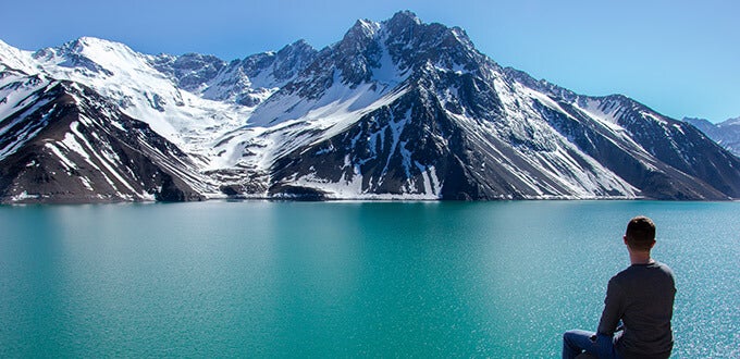 Persona contemplando el Embalse El Yeso entre montañas nevadas, paisaje andino del Cajón del Maipo, Región Metropolitana, Chile.