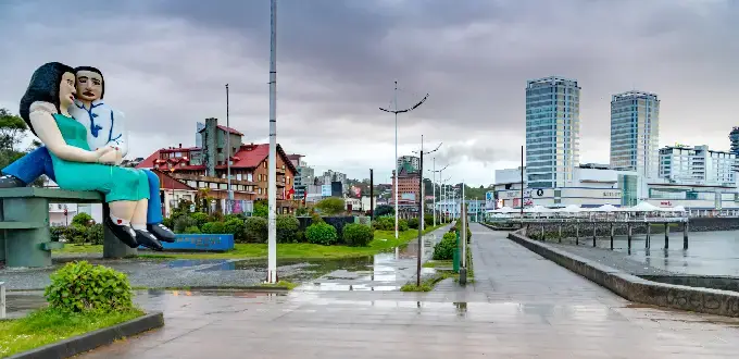 Escultura Sentados Frente al Mar en Puerto Montt, Chile, con costanera, lluvia y edificios frente al mar