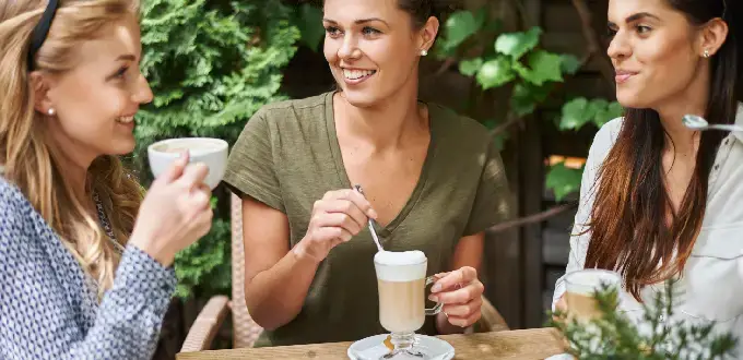 Amigas disfrutando café al aire libre en una terraza con jardín, ideal para compartir y relajarse.