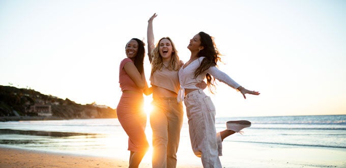 Tres amigas saltando y celebrando al atardecer en la playa, verano, amistad, viaje, libertad, alegría frente al mar.