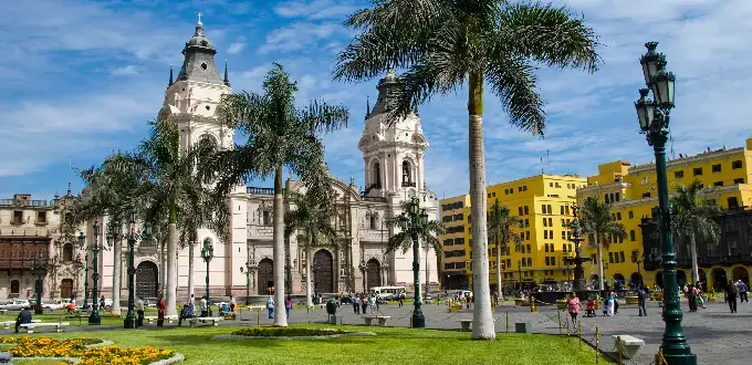 Catedral de Lima, Perú, rodeada de palmeras, jardines y edificios históricos en la Plaza Mayor.