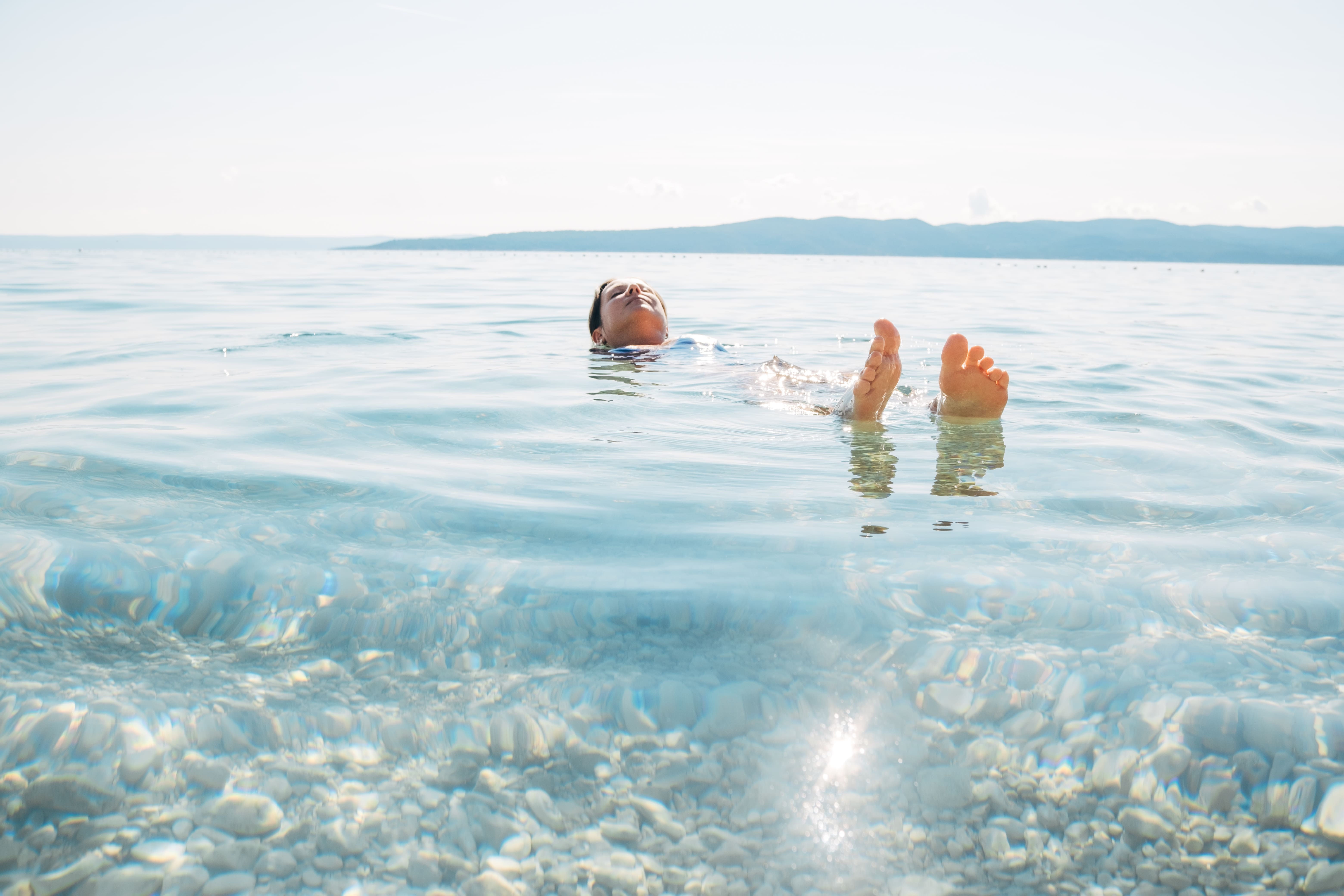 Persona flotando plácidamente en el mar cristalino de colombia con fondo de piedras blancas y montañas a lo lejos.