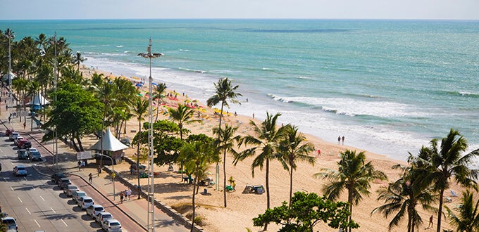 Playa de Boa Viagem en Recife, Brasil, con palmeras, arena dorada, aguas verdes y un concurrido paseo costero junto a la avenida.