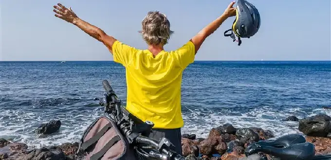 Hombre junto al mar con bicicleta, brazos en alto frente al océano Pacífico, escena de libertad y aventura en la costa de Chile.