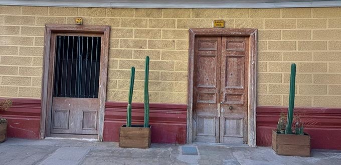 Fachada tradicional en Chile con muros de adobe, puertas de madera y cactus en macetas, arquitectura rural y patrimonial.