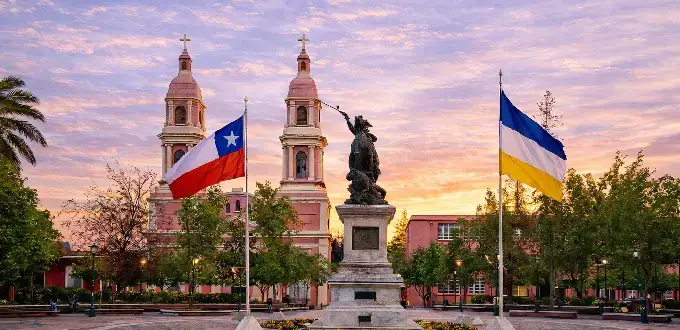 Plaza de los Héroes en Rancagua, Chile, con el Monumento a O’Higgins, banderas y la Catedral al atardecer.