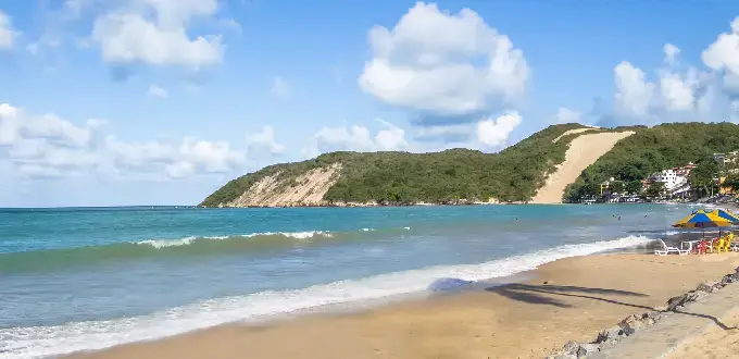 Playa Ponta Negra con el Morro do Careca al fondo, aguas turquesas y arena dorada en Natal, Brasil.
