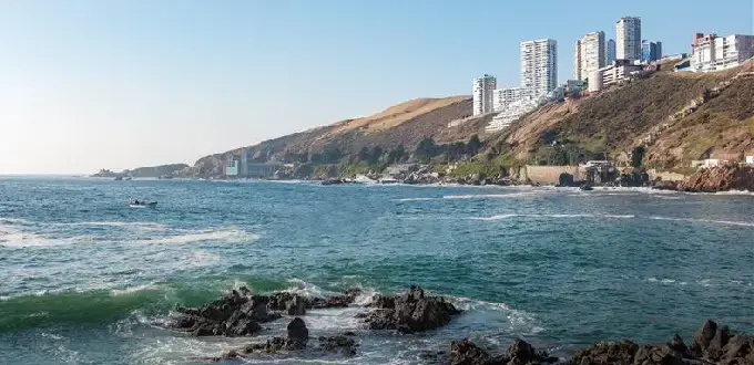 Vista de la costa de Concón, Región de Valparaíso, con edificios en los cerros, rocas en el mar y olas del océano Pacífico.