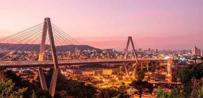 Puente atirantado y vista urbana de Pereira, Colombia, al atardecer con montañas y luces de la ciudad.
