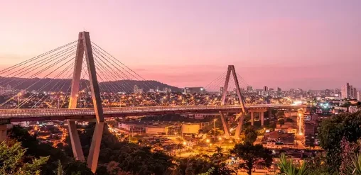 Puente atirantado y vista urbana de Pereira, Colombia, al atardecer con montañas y luces de la ciudad.
