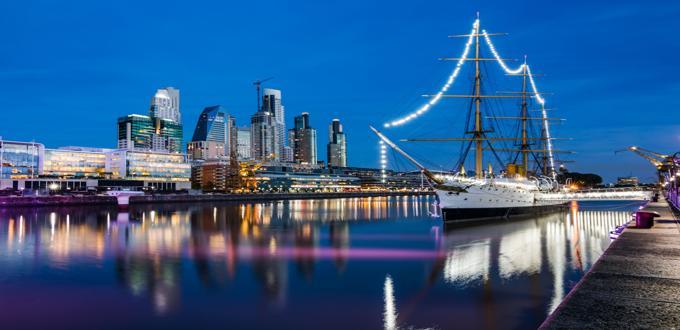 Velero iluminado en el dique de Puerto Madero con rascacielos modernos al fondo, en Buenos Aires.