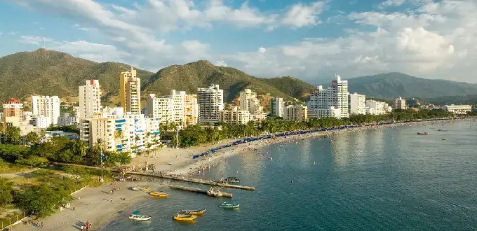 Playa El Rodadero en Santa Marta, Colombia, con edificios costeros, mar Caribe y montañas al fondo.