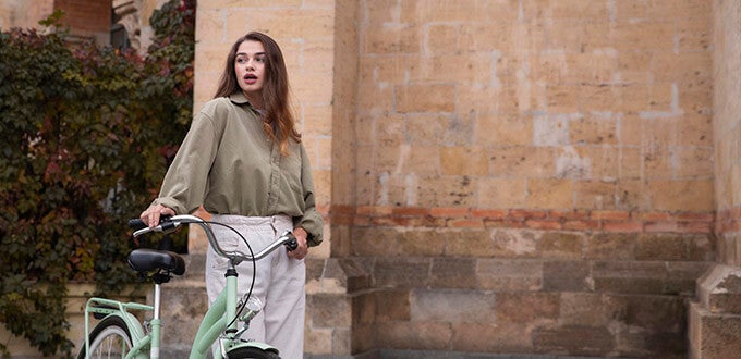 Mujer recorre la ciudad en bicicleta junto a un muro patrimonial, reflejando turismo urbano, estilo de vida y exploración cultural.