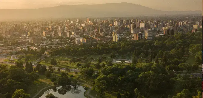 Vista panorámica de San Miguel de Tucumán, Argentina, con parques, edificios y sierras al fondo.