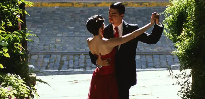 Pareja bailando tango en San Telmo, Buenos Aires, rodeada de vegetación y adoquines clásicos.