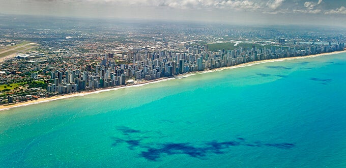 Vista aérea de Recife, Brasil, con rascacielos frente al mar turquesa, extensas playas y contraste urbano costero.