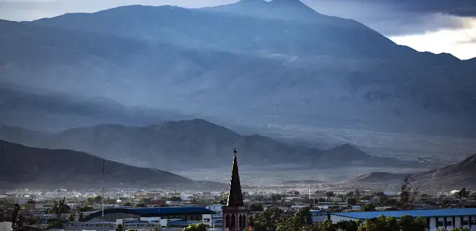 Vista de Calama en el desierto de Atacama, con iglesia, ciudad y cordillera de los Andes al fondo bajo cielo nublado