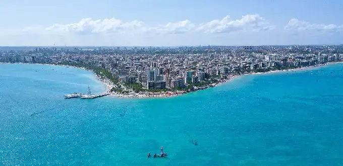 Vista aérea de Maceió, Brasil, con costa urbana, playas de aguas turquesas y edificios frente al mar.