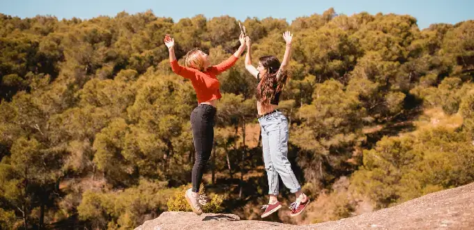 Amigas haciendo trekking en Olmué, Chile, saltando sobre rocas con bosque nativo de fondo.