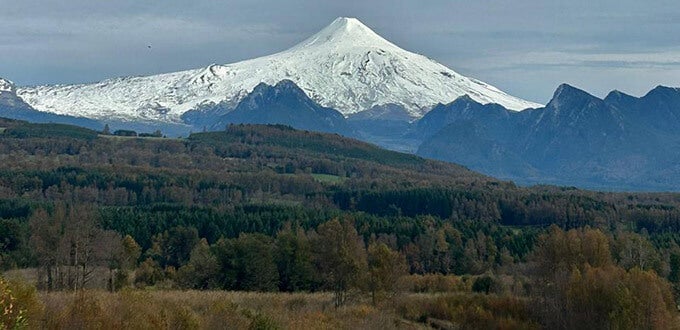 Volcán Villarrica cubierto de nieve sobre bosques del sur de Chile, paisaje natural de Pucón, Región de La Araucanía.