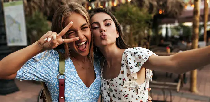 Amigas felices tomándose una selfie en Buenos Aires, con gesto de paz y ambiente urbano al atardecer
