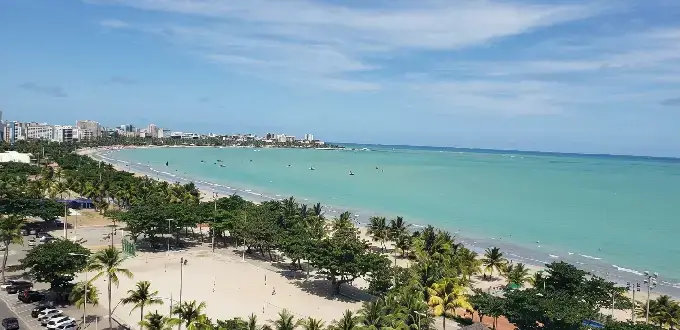 Praia de Pajuçara en Maceió, Brasil, con mar turquesa, arena blanca, palmeras y paseo costero urbano.