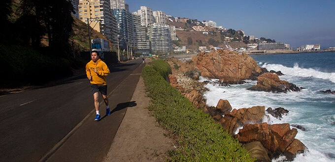 Personas corren por el borde costero con vista al mar y roqueríos, actividad deportiva en Playa Reñaca, Viña del Mar, Chile.