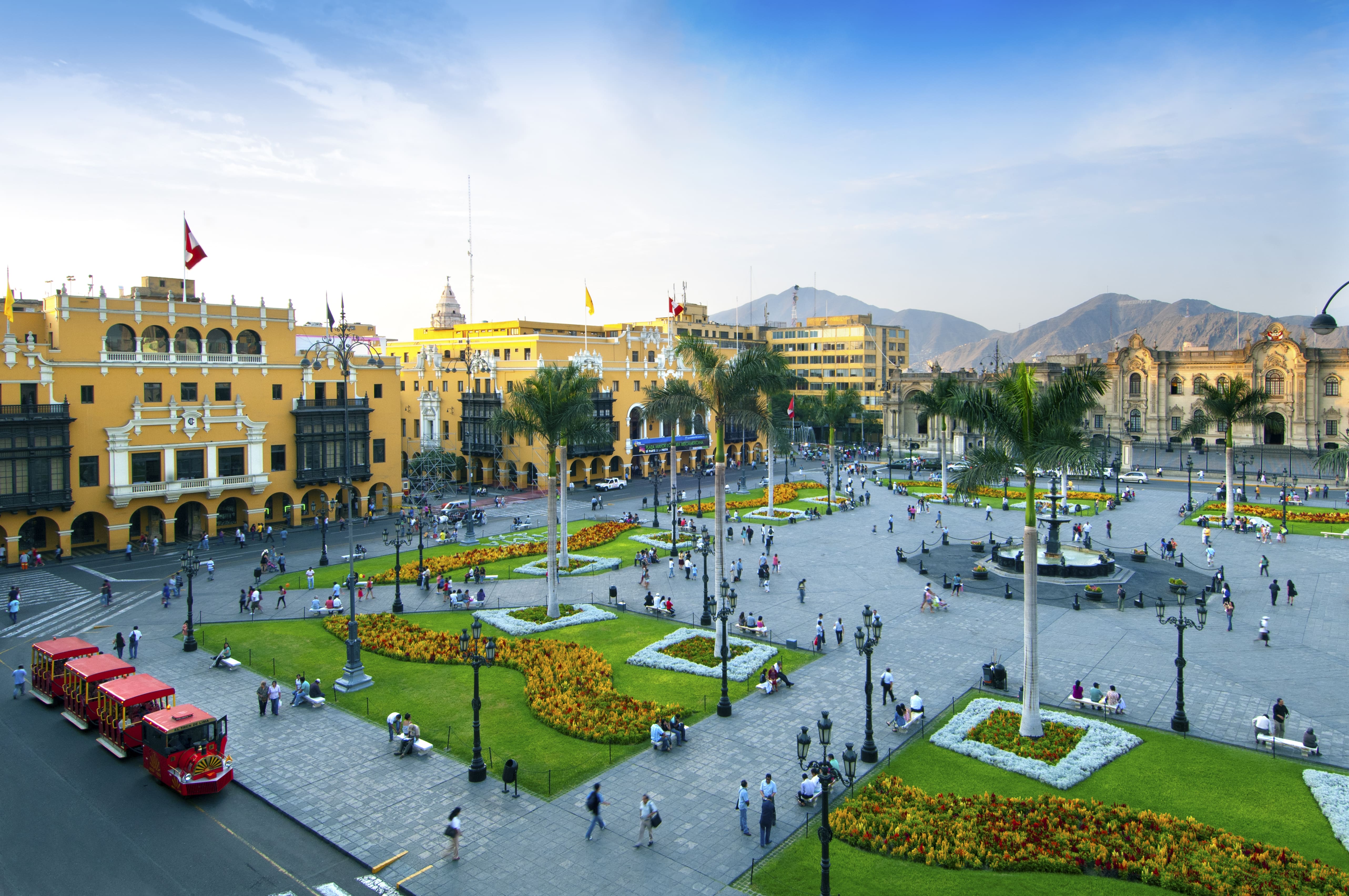 Plaza Mayor de Lima durante el día, con jardines, palmeras y edificios coloniales en el Centro Histórico de la ciudad.