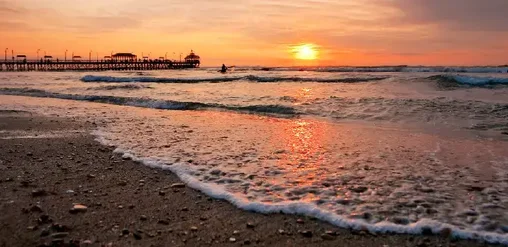 Playa Huanchaco, Trujillo, Perú, con atardecer sobre el mar y tradicional muelle costero.