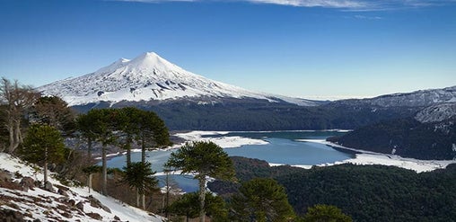 Volcán Llaima nevado sobre bosques de araucarias y lagunas del parque nacional, Conguillío, región de La Araucanía, Chile.