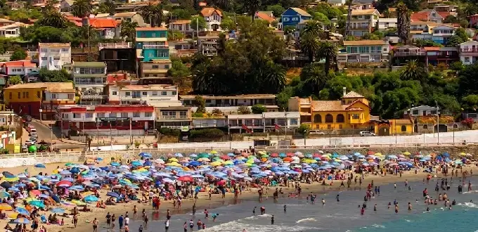 Playa San Antonio llena de sombrillas, turistas y casas coloridas frente al mar.