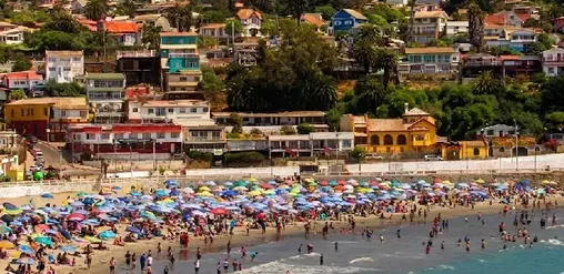 Playa San Antonio llena de sombrillas, turistas y casas coloridas frente al mar.