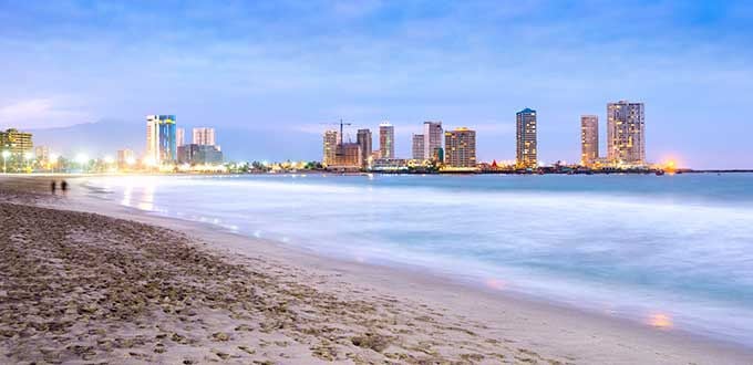 Iquique, Chile: playa urbana al atardecer con arena clara, mar tranquilo y skyline iluminado frente al Pacífico.