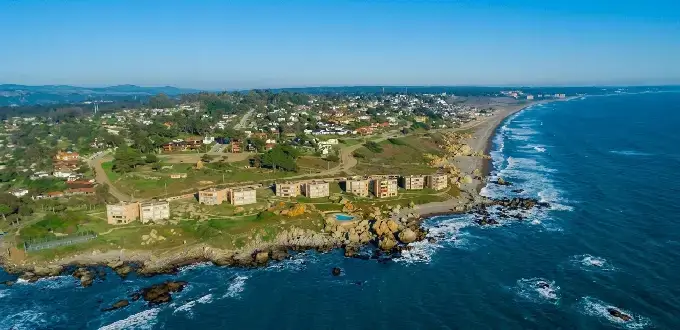 Vista aérea de Santo Domingo, Chile, con costa rocosa, playa, edificios y océano Pacífico.