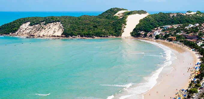 Playa de Ponta Negra en Natal, Brasil, con aguas turquesa, arena clara y el Morro do Careca cubierto de verde y su imponente duna.