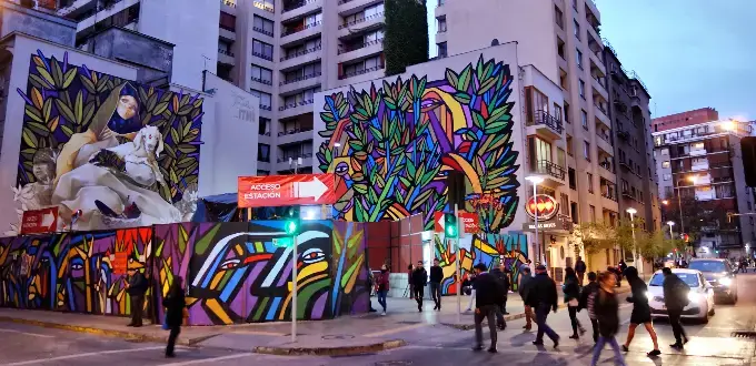 Murales de arte urbano y peatones en una esquina del barrio Bellavista, Santiago de Chile, al atardecer.