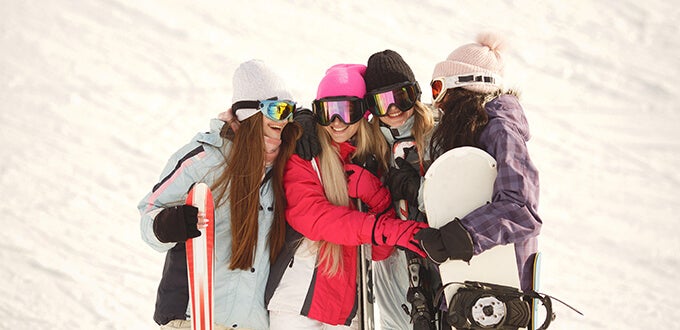 Grupo de amigas disfruta la nieve con equipos de ski y snowboard, jornada invernal en centro de montaña de la Cordillera de los Andes, Chile.