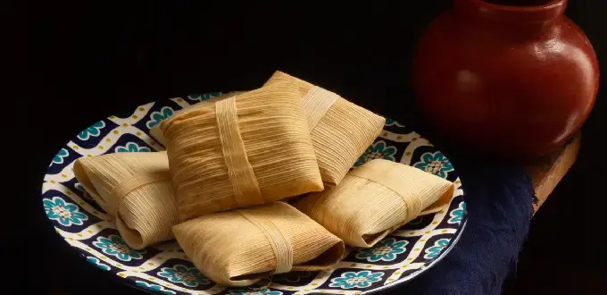 Tamales, comida típica de Tucumán, Argentina, servidos en un plato artesanal junto a una vasija de barro.