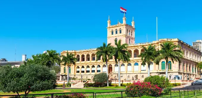 Palacio de López en Asunción, Paraguay, rodeado de jardines, palmeras y arquitectura histórica bajo un cielo despejado.