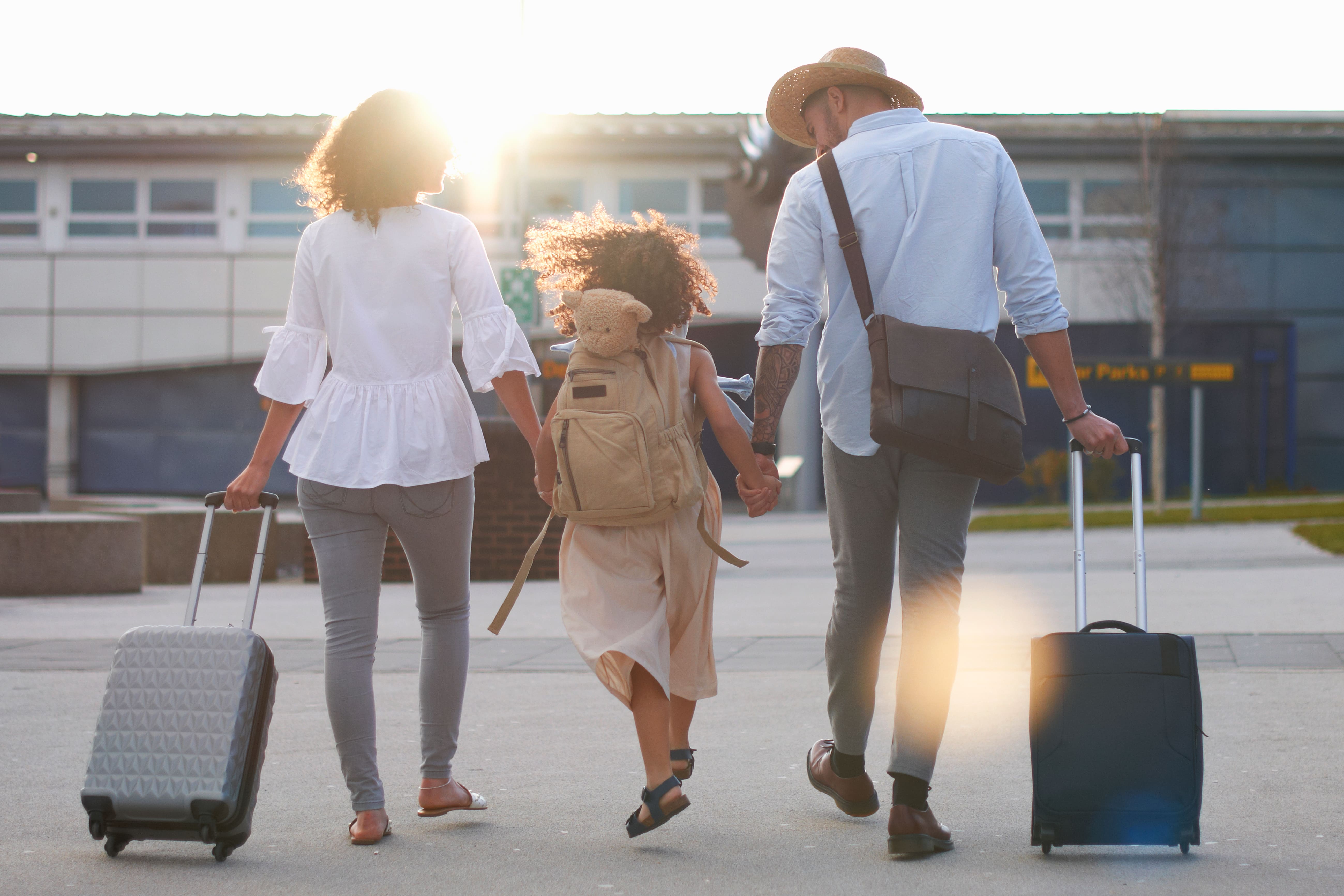 Familia caminando con maletas y mochila infantil al salir del aeropuerto, listos para iniciar su viaje.