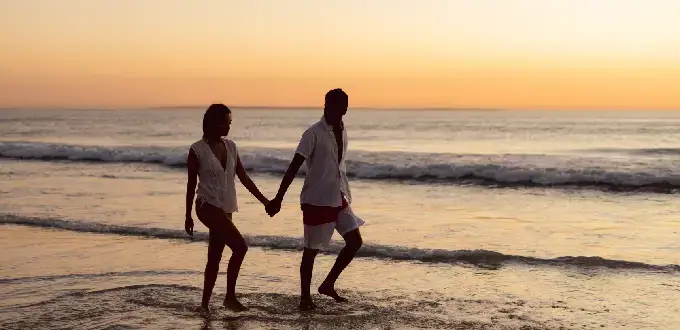 Pareja caminando al atardecer por la playa en Viña del Mar, Chile, con olas del Pacífico y cielo dorado.