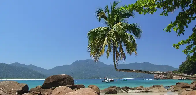 Playa Lopes Mendes en Ilha Grande, Brasil, con aguas turquesas, palmeras y montañas de fondo.
