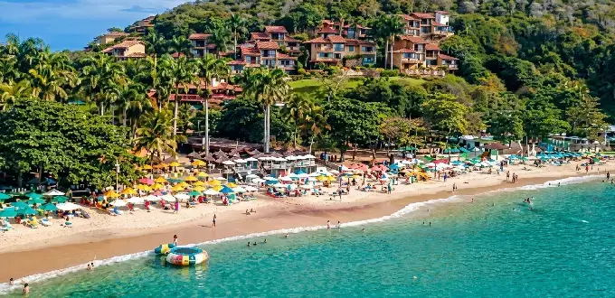 Playa de Búzios, Brasil, con aguas turquesas, arena clara, palmeras y costa rodeada de naturaleza.
