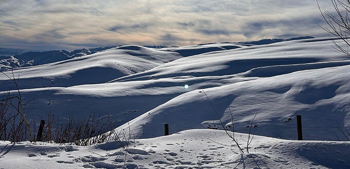 Paisaje de montañas cubiertas de nieve con suaves colinas y cielo nublado, típico invierno en Farellones, cordillera de Chile.