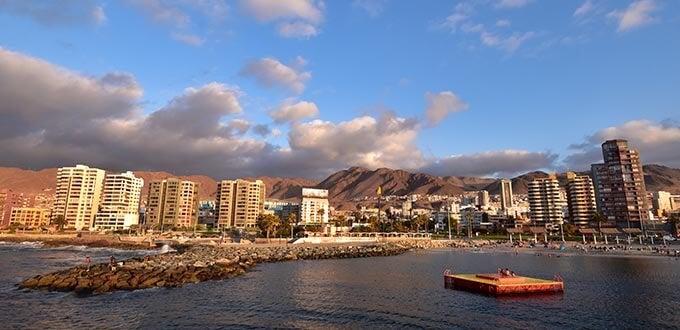Antofagasta, Chile: vista costera al atardecer con edificios frente al mar, cerros del desierto y aguas tranquilas del Pacífico.