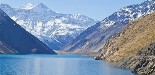 Embalse de aguas turquesas rodeado de montañas nevadas y rocosas en la cordillera de los Andes, Cajón del Maipo, Chile.