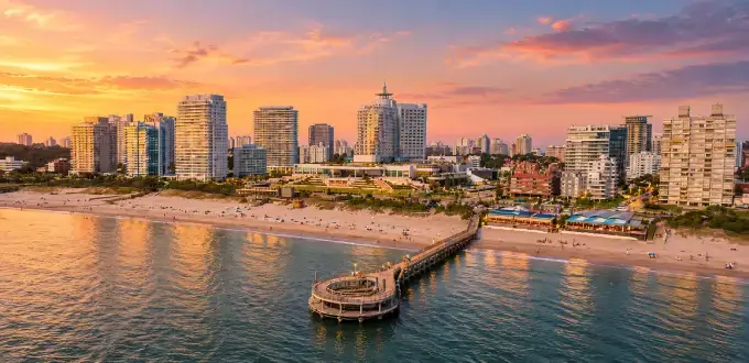 Vista aérea de Punta del Este, Uruguay, con playa, muelle, edificios costeros y un atardecer sobre el mar.
