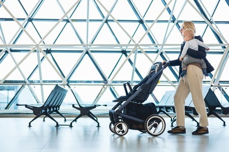 Madre caminando por un aeropuerto con un bebé y un coche de bebé antes de abordar un vuelo.