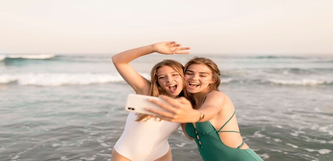 Dos amigas sonríen y se toman una selfie en la orilla del mar, ambiente veraniego y turístico en Playa Reñaca, Viña del Mar, Chile.