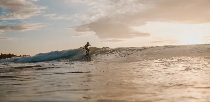 Surf en Florianópolis, Brasil, con una persona surfeando una ola al atardecer y el mar como escenario natural.
